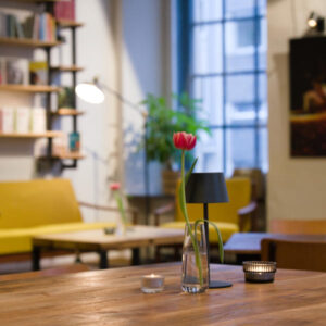 Blumenvase auf einem Tisch vor der beleuchteten Bühne im VERS-Literaturcafé