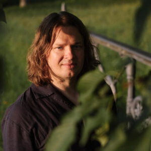 Der Autor Jan Snela mit schulterlange Haaren in der Natur. Bild: © Maximilian Gödecke Photography